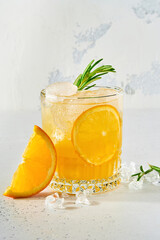 Orange juice or cocktail with rosemary and orange with ice in glass, cold summer lemonade on light gray slate, stone or concrete background. Beach concept with deep sun shadow. Top view.