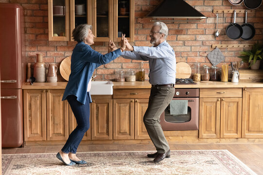 Cook with a twist. Active aged family couple enjoy cooking dancing at modern designed wooden kitchen distracted of preparing meals. Energetic older spouses have dance party for two at country cottage