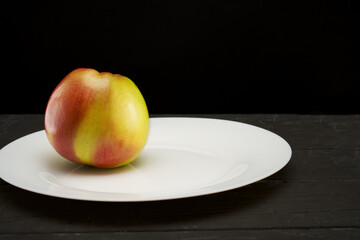 Apple on a white plate on a black background on a black wooden table