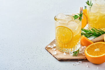 Orange juice or cocktail with rosemary and orange with ice in glass, cold summer lemonade on light gray slate, stone or concrete background. Beach concept with deep sun shadow. Top view.