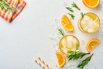 Orange juice or cocktail with rosemary and orange with ice in glass, cold summer lemonade on light gray slate, stone or concrete background. Beach concept with deep sun shadow. Top view.