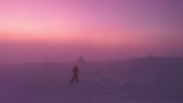 Aerial view of Santa walking on a mountain colorful, hazy winter sunset - pan drone shot