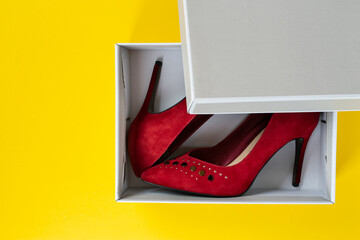New women's red suede shoes in a box on a yellow background. Top view.
