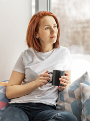 portrait of young woman with cup of coffee in her hands sitting near the window