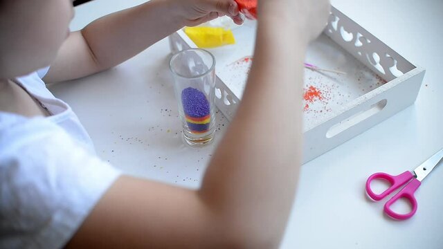 a girl girl sprinkles paraffin with a spoon makes makes a candle from small paraffin granules. kids pens are lying on a white table granules. Paraffin montessori material scissors, candle cup, wick. c