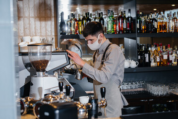 A masked barista prepares delicious coffee at the bar in a cafe. The work of restaurants and cafes during the pandemic.