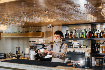 Submission of a Barista in a mask of delicious organic coffee in modern cafe during the pandemic.