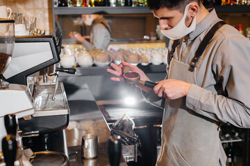 Close-up of a masked barista preparing a delicious coffee at the bar in a cafe. The work of restaurants and cafes during the pandemic.