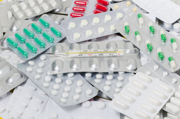 A pile of medical pills and capsules and a thermometer