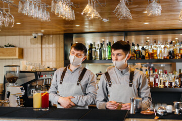 Two stylish bartenders in masks and uniforms during the pandemic, preparing cocktails. The work of restaurants and cafes during the pandemic.
