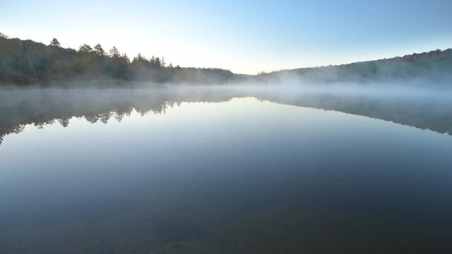 Wide angle view of Spruce Knob Lake in Appalachian mountains of Canaan valley in West Virginia with sunrise morning mist fog floating above water in Monongahela National Forest in autumn fall season