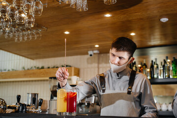 Two stylish bartenders in masks and uniforms during the pandemic, preparing cocktails. The work of restaurants and cafes during the pandemic.