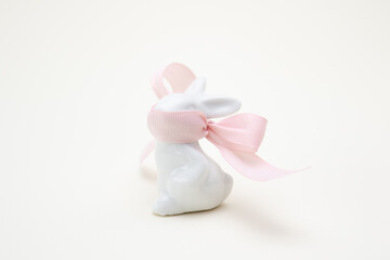 A porcelain rabbit with a pink ribbon covering its muzzle on a light yellow background. Easter decoration