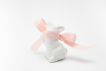 Porcelain rabbit with a pink ribbon covering the muzzle on a white background. Easter decoration