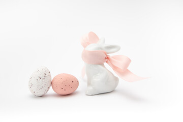 Two chocolate eggs, white and red with specks on a white background. Imitation of quail eggs. Porcelain rabbit with a pink ribbon covering the muzzle