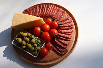 Salami cheese board with tomatoes and green olives on white table background. Set of appetizers. Flat lay food. Top view, copy space