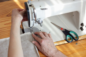 Obraz na płótnie Canvas Middle aged woman hands sewing linen cloth on stitching machine, from above overhead top view, handicraft, slow fashion,everyday life moments and eco lifestyle concept