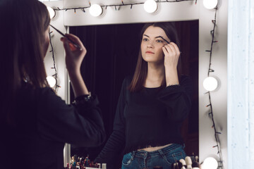 Woman looking into a mirror. Makeup artist woman doing make-up using cosmetic brush for yourself