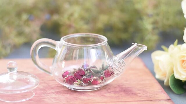 A beautiful sophisticated female hand throws small roses into a small teapot. Pink rose tea with boiling water. Aesthetic delicate content, good morning.