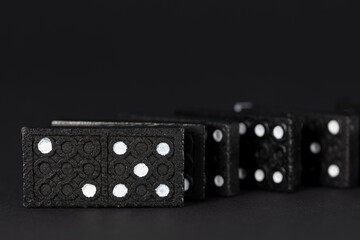 Several dominoes stand one behind the other in front of a dark background