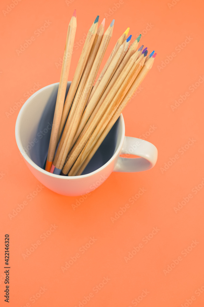 Poster Top view closeup of colored pencils put in a white mug on an orange background