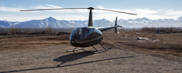 Small helicopter is parked on a dirt platform against the backdrop of mountains. © okyela