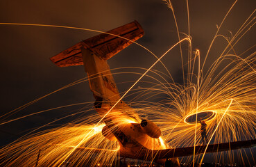 Fire show, swirl, steel wool. Sparks from a metal. Old plane on the hill. Night landscape with light effects.