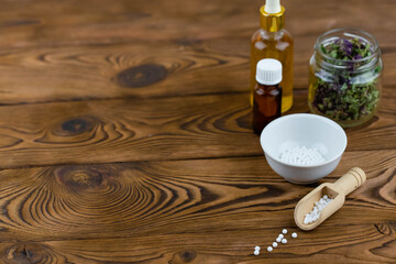 Homeopathy alternative medicine eco concept - classical homeopathy pills. Homeopathic globules, natural organic aroma oil essence and healing herbs. Wooden background. 