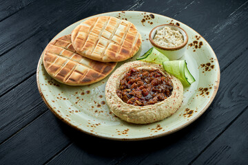 A classic oriental dish - chickpea hummus with baked vegetables and olive oil served with baked pita in a plate on a dark wood background. Vegetarian food. Diet