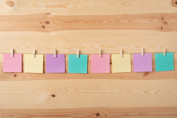 Blank multicolored papers hanging with the help of clothespin on a rope. Row of sheets for notes on wooden background.