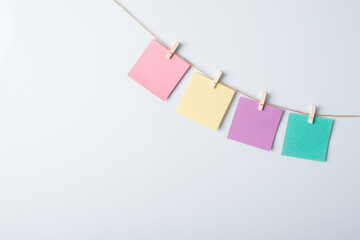 Pieces of multicolored paper hang on a rope with the help of clothespins. White background, copy space, frame.