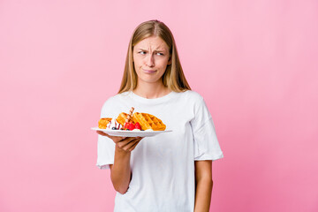 Young russian woman eating a waffle isolated confused, feels doubtful and unsure.