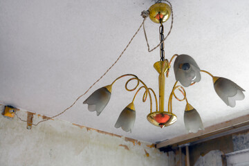 Old and unsafe chandelier in a run-down flat of a panel house
