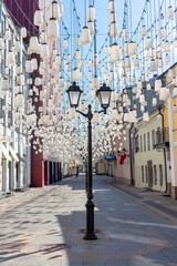 Obraz premium Decorations of Stoleshnikov lane in Moscow. Large garland from electric bulbs hangs above pedestrian street. Clear blue sky in the background. Travel in Russia theme.