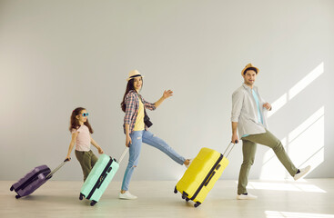 Naklejka premium Family goes on summer vacation. Cheerful mom, dad and their daughter have fun walking with suitcases along the gray wall. Concept of active family, travel and summer vacations. Banner.