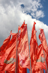 Group of red flags with george ribbons swings on flagpoles. Blue sky with few clouds in the background. Russian Victory day holiday theme.