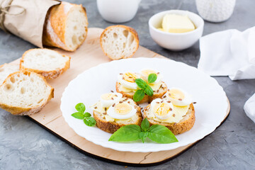 Hearty breakfast in the morning. Fresh baguette sandwiches with butter, quail eggs, flax seeds and basil seeds on a plate on the table