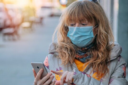 adult woman with mask and mobile phone on city street outdoors