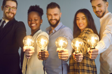 Happy creative team holding glowing lit lightbulbs. Diverse collaboration group of intelligent...