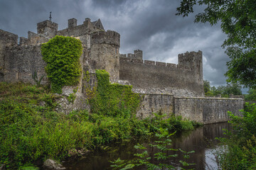 Fototapeta na wymiar Ancient fortification covered in green ivy, with moat, Cahir castle in Cahir town with dramatic, storm sky in background, County Tipperary, Ireland