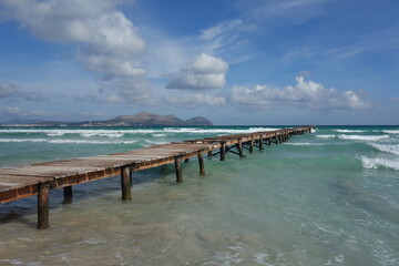 Long old wooden pier reaching out to the Mediterranean sea on a sunny windy day