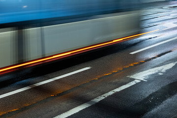 Long exposure wet road with light trails and bus passing at rainy night