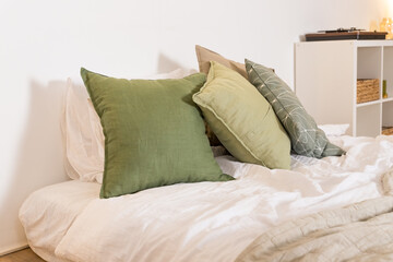 modern bedroom with green pillows on bed.Comfortable bed with new pistachio Cushions , beige and white linens in modern room interior.