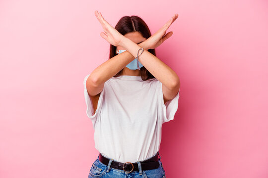 Young caucasian woman wearing a mask for virus isolated on pink background keeping two arms crossed, denial concept.