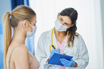Naklejka premium Doctor in mask explaining diagnosis to her female patient