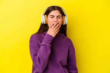 Young caucasian woman listening to music with headphones isolated on pink background yawning...