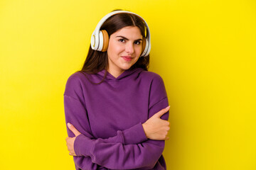 Young caucasian woman listening to music with headphones isolated on pink background who feels confident, crossing arms with determination.