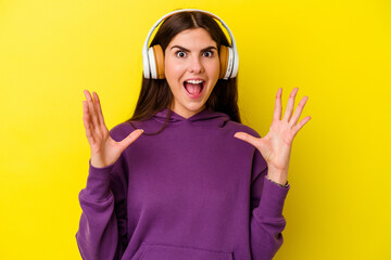 Young caucasian woman listening to music with headphones isolated on pink background celebrating a victory or success, he is surprised and shocked.