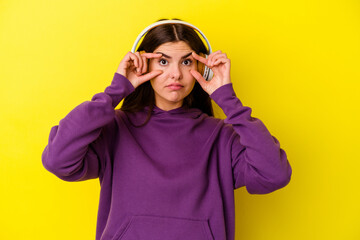 Young caucasian woman listening to music with headphones isolated on pink background keeping eyes opened to find a success opportunity.