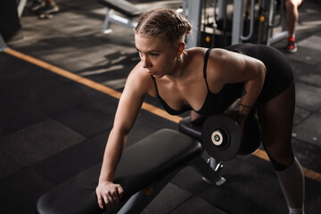 Fototapeta na wymiar Attractive young sportswoman doing dumbbell row at the gym, copy space